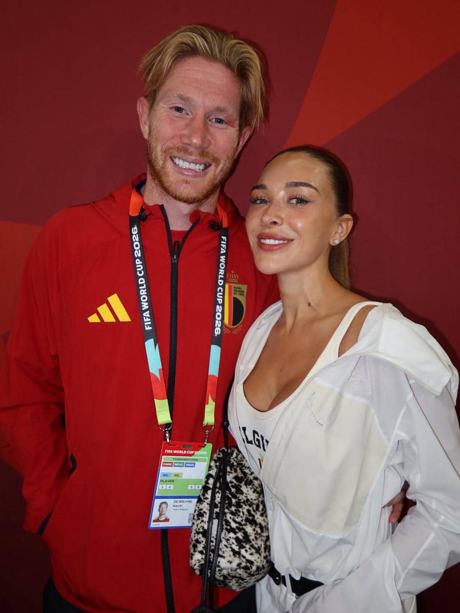 Seorang pemain tim nasional Belgia mengenakan jaket merah berpose bersama pasangannya yang mengenakan jaket putih di ajang Piala Dunia 2026.