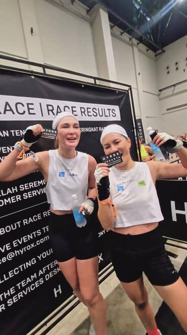 Dua peserta wanita mengenakan pakaian olahraga putih dan hitam berpose sambil memegang botol minuman setelah lomba HYROX Jakarta 2026.