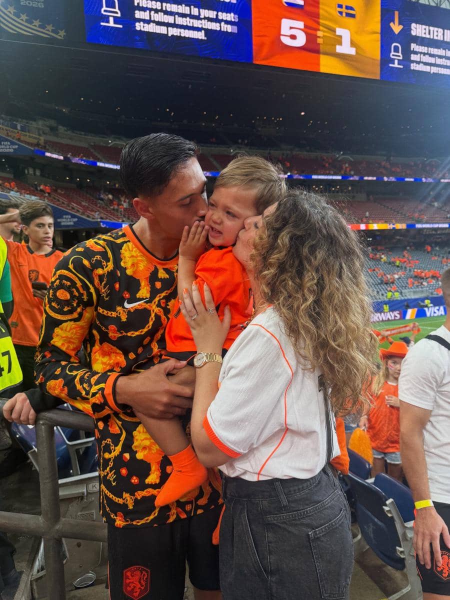 Seorang pemain sepak bola mengenakan jersey oranye hitam mencium anak kecil di stadion bersama seorang wanita setelah pertandingan Piala Dunia 2026.