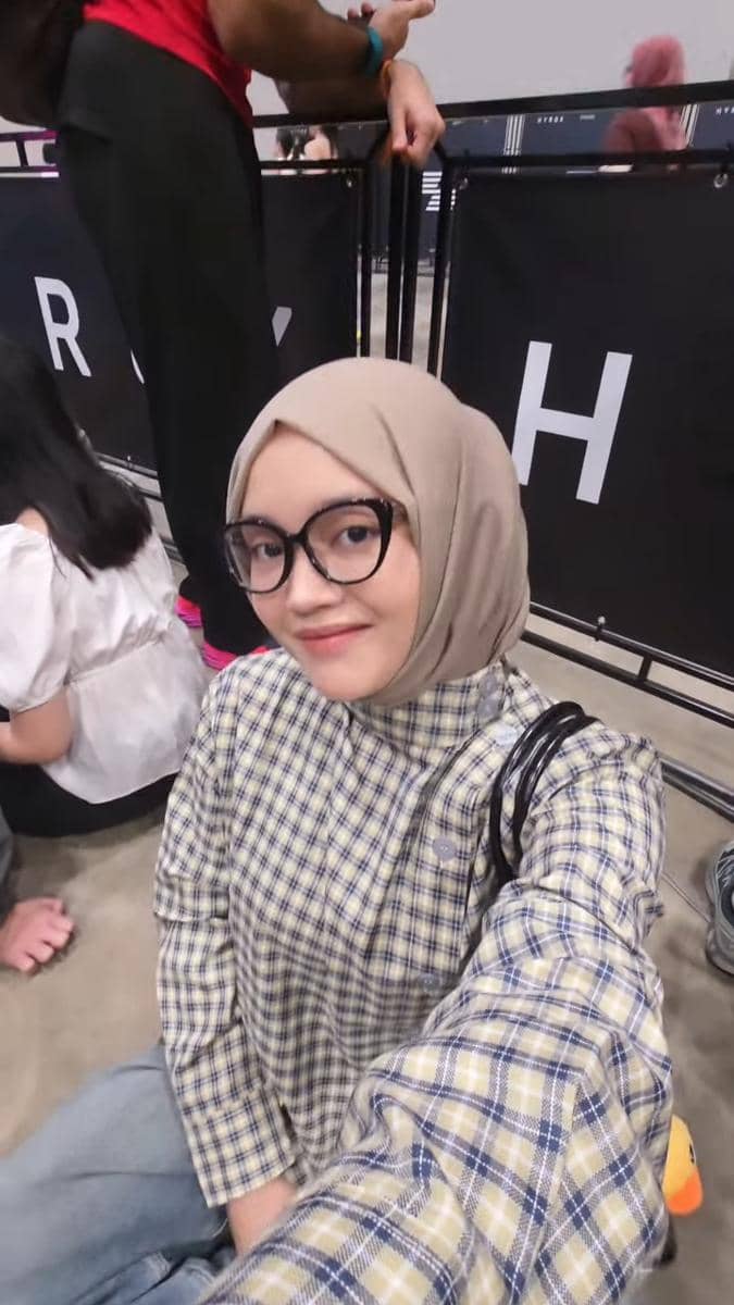 Seorang perempuan berhijab dan berkacamata berpose selfie di area penonton acara HYROX Jakarta 2026 Day 2.