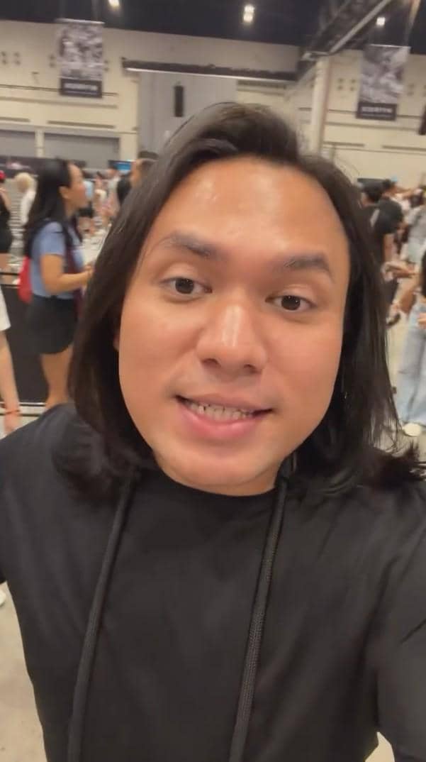 Seorang pria berambut panjang mengenakan kaus hitam sedang berfoto selfie di acara HYROX Jakarta 2026 Day 2 dengan latar ramai pengunjung.