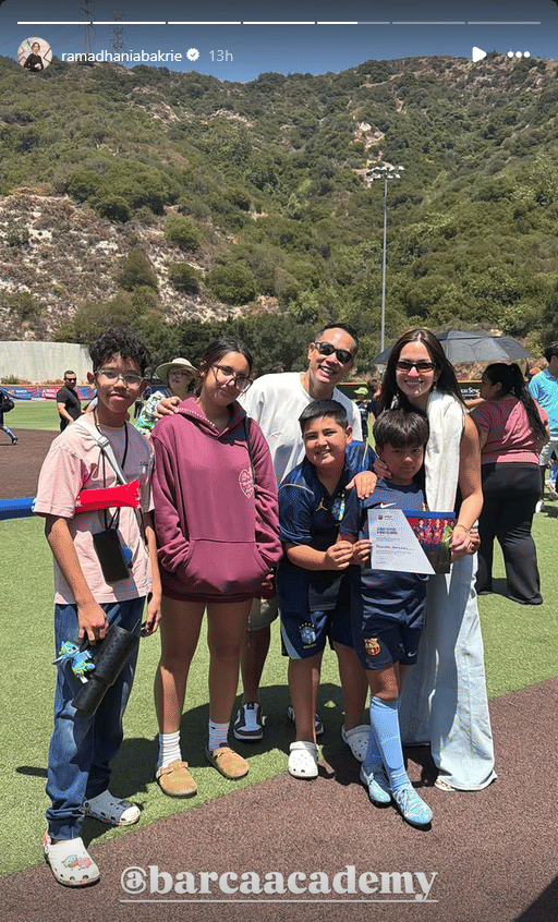 Keluarga berpose di lapangan sepak bola luar ruangan dengan dua anak mengenakan seragam Barcelona Academy sambil memegang sertifikat.