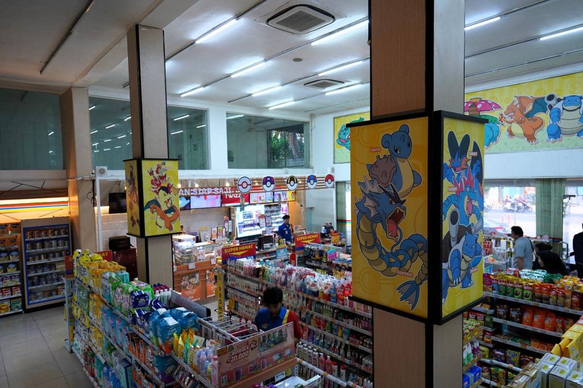 Suasana dalam toko Indomaret bertema Pokemon dengan dekorasi karakter di dinding dan tiang serta berbagai produk di rak.