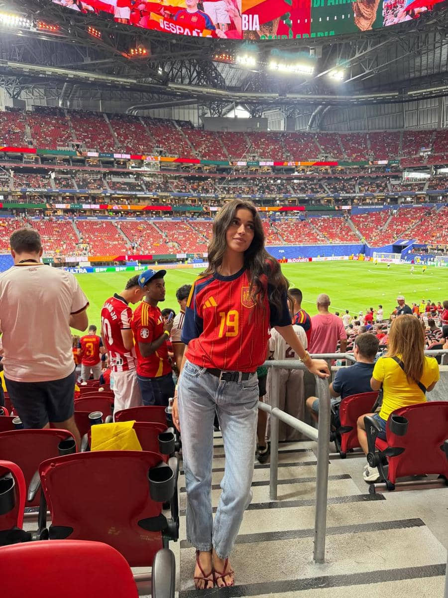 Seorang perempuan mengenakan jersey tim nasional Spanyol berdiri di tribun stadion yang dipenuhi penonton selama pertandingan Piala Dunia 2026.