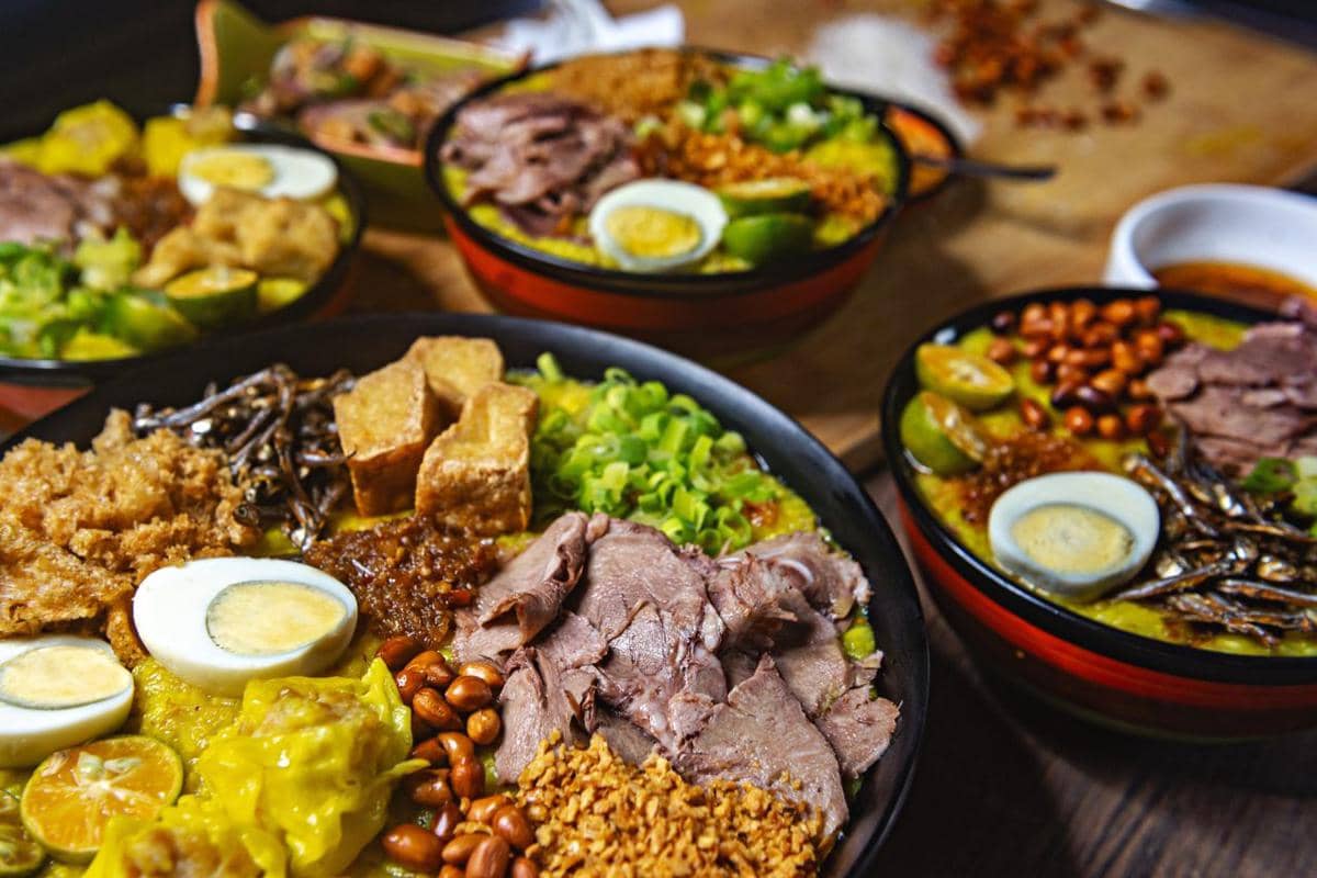 Semangkuk bubur dengan berbagai topping seperti telur rebus, daging iris, tahu goreng, kacang tanah, dan irisan jeruk nipis.