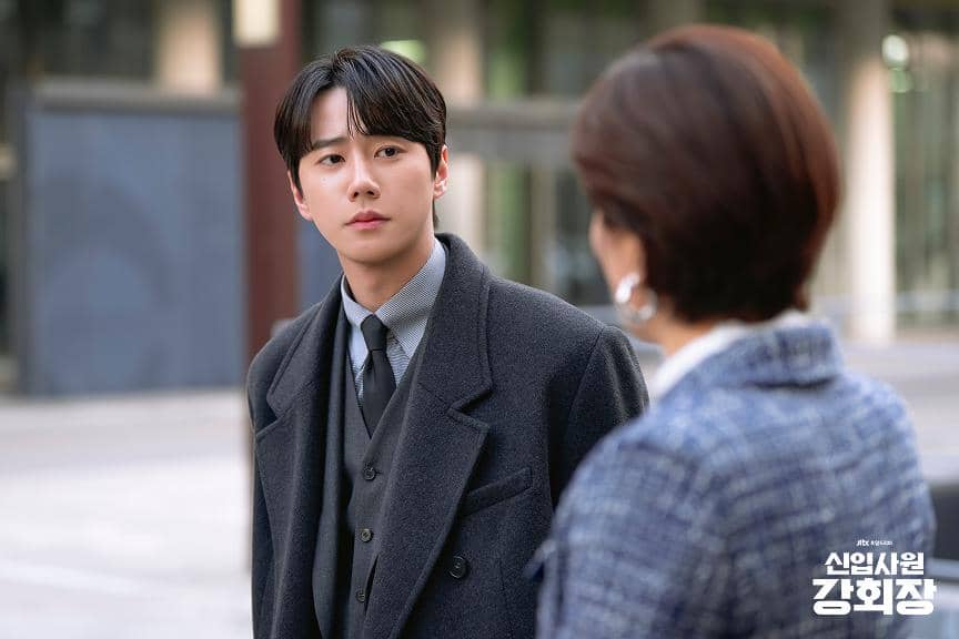 Seorang pria mengenakan jas abu-abu berbicara dengan seorang wanita berambut pendek di luar gedung dalam cuplikan drama Korea Reborn Rookie.