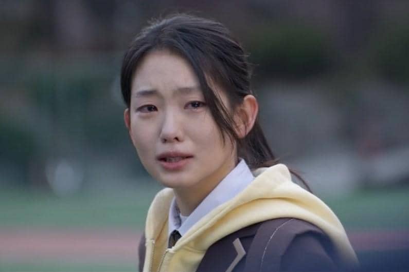 Seorang perempuan muda mengenakan seragam sekolah dan jaket kuning tampak sedih di luar ruangan dalam cuplikan drama Agent Kim Reactivated.