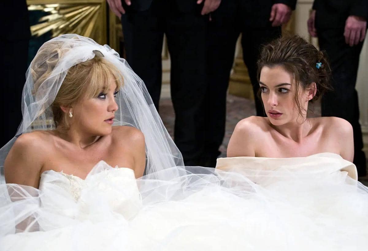 Dua wanita mengenakan gaun pengantin putih saling menatap dengan ekspresi tegang dalam adegan film Bride Wars.