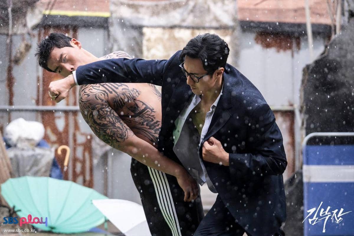 Adegan pertarungan intens di bawah hujan antara dua pria, salah satunya bertelanjang dada dengan tato besar, dari drama Agent Kim Reactivated.