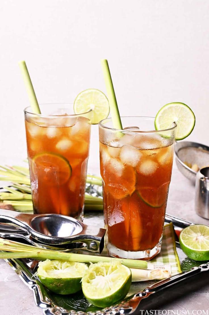 Segelas es teh serai jeruk dengan irisan jeruk nipis dan batang serai, disajikan dingin sebagai minuman menyegarkan.