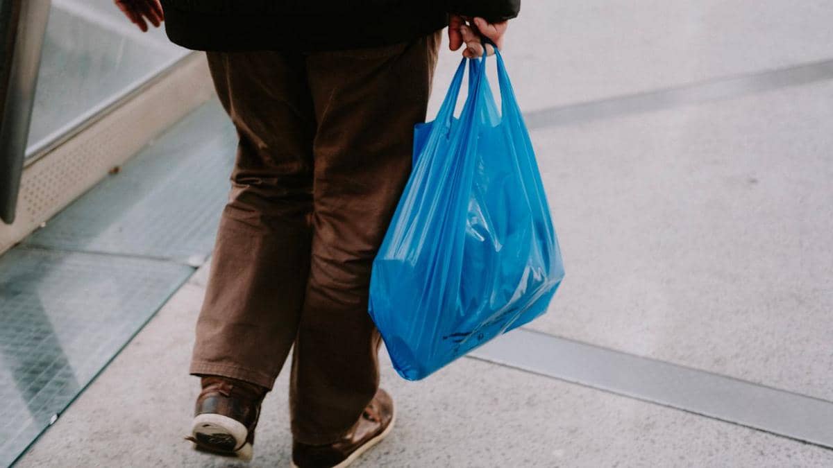 Ilustrasi tangan seseorang membawa kantong plastik belanja berisi barang saat berada di area luar ruangan.