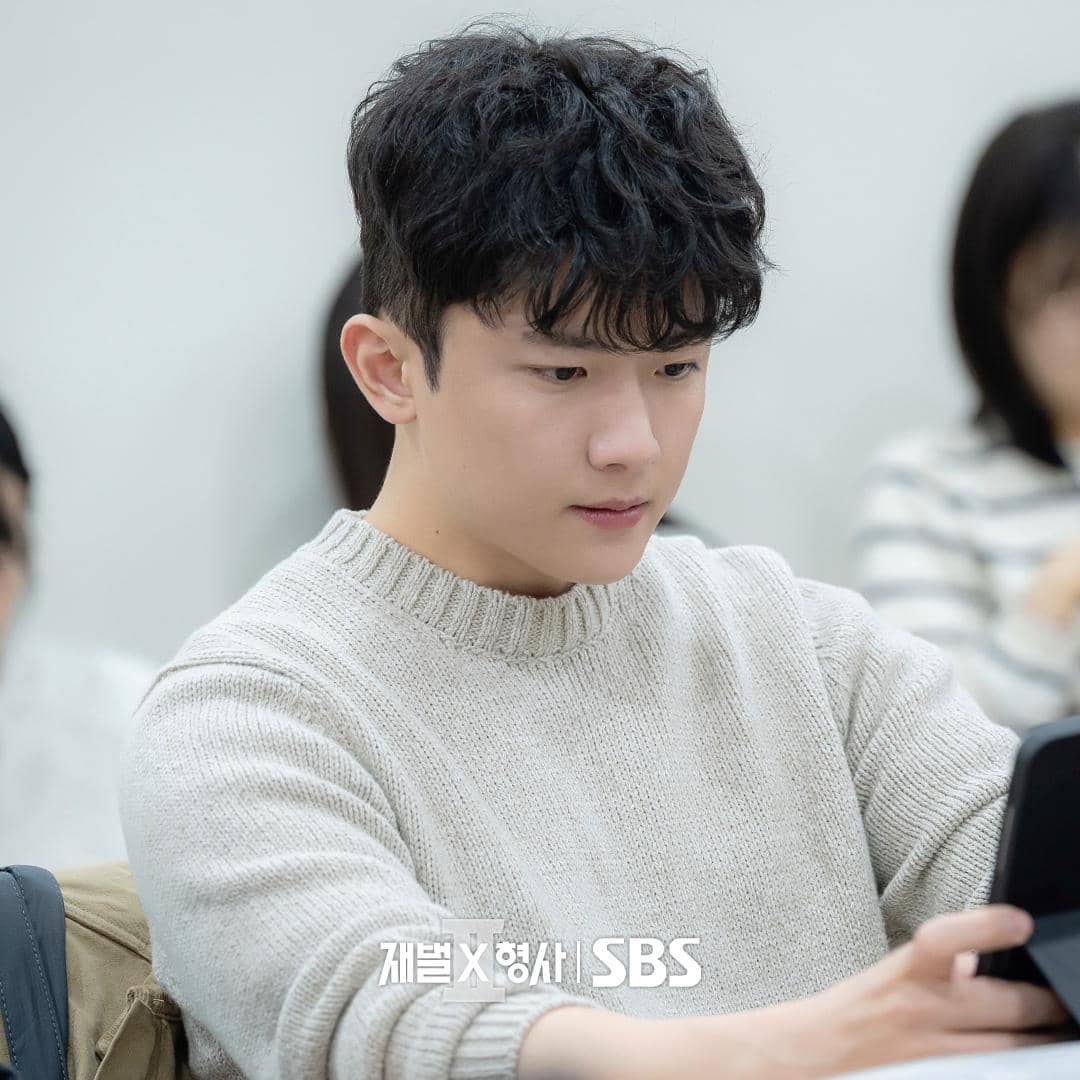 Seorang aktor mengenakan sweater rajut berwarna krem sedang membaca naskah dalam sesi pembacaan naskah drama Flex X Cop 2.