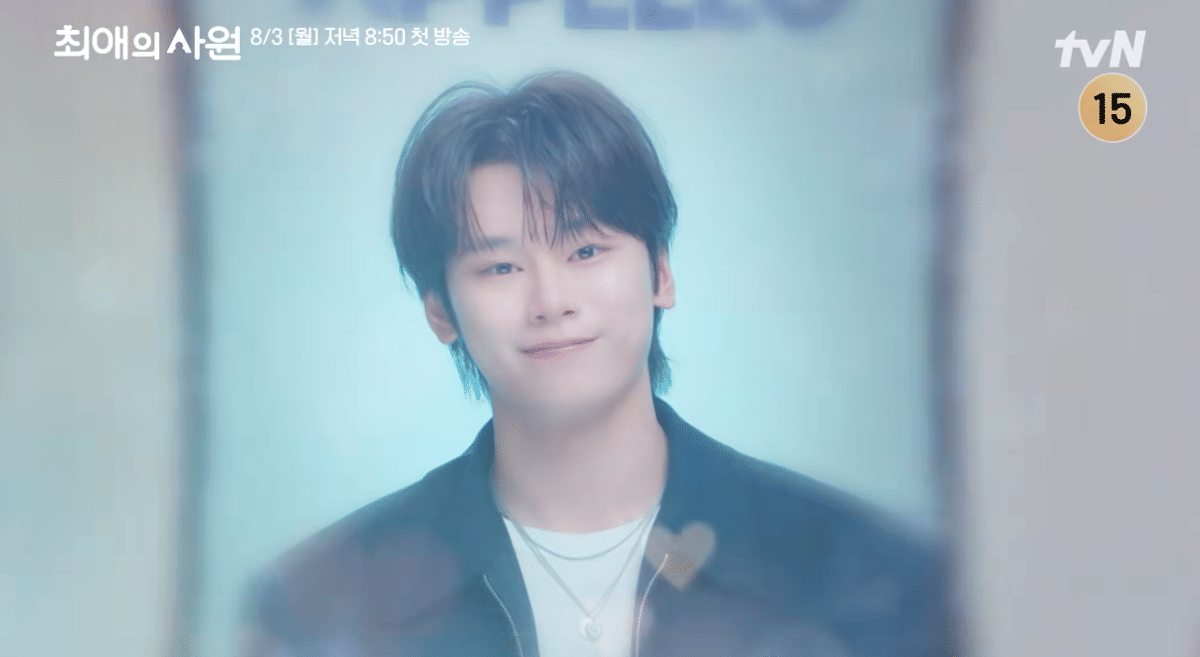Seorang pria muda tersenyum lembut mengenakan jaket hitam dan kalung perak dalam cuplikan drama My Bias, My Boss dari tvN.