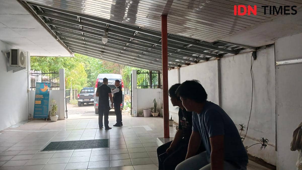 Beberapa orang berada di area parkir RS Bhayangkara Manado dengan ambulans terparkir di luar ruangan pada siang hari.