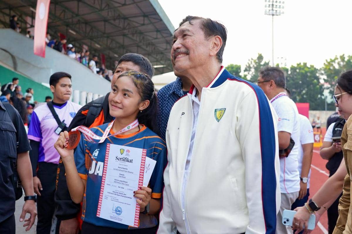 Seorang atlet muda memegang medali dan sertifikat sambil berfoto bersama seorang pria di arena Kejurnas Atletik Indonesia U-18.