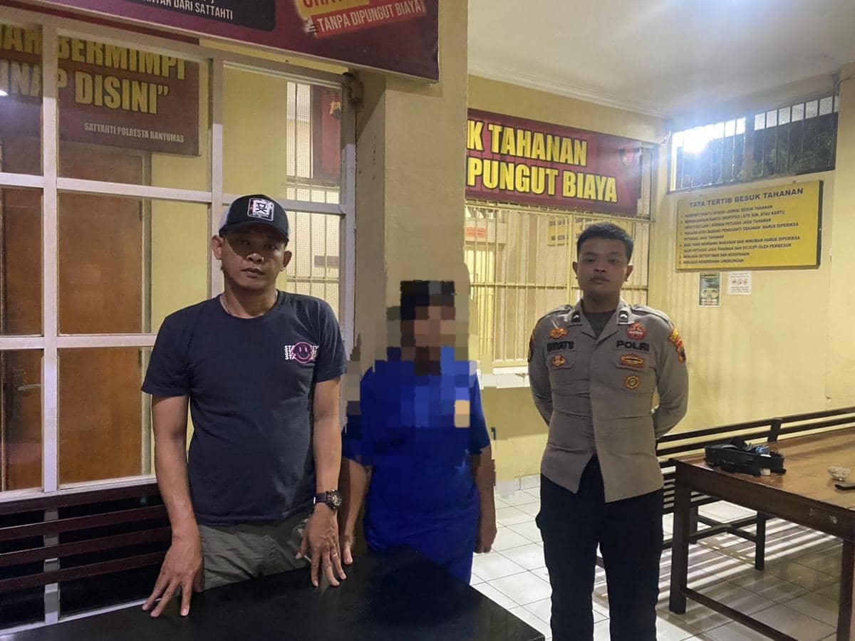 Petugas kepolisian Polresta Banyumas berdiri bersama seorang perempuan berpakaian biru yang diduga pelaku di ruang tahanan.