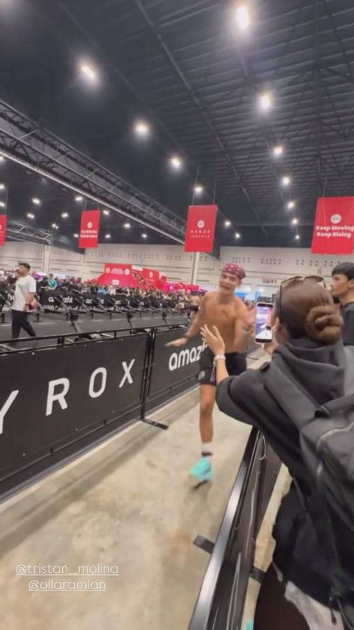 Seorang pria berlari tanpa baju di arena kompetisi HYROX Jakarta 2026 sambil disemangati oleh seorang wanita di tepi lintasan.