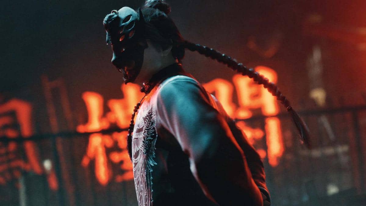 Karakter Bakunawa Killer bertopeng dengan rambut kepang panjang berdiri di latar belakang bercahaya merah neon yang misterius.
