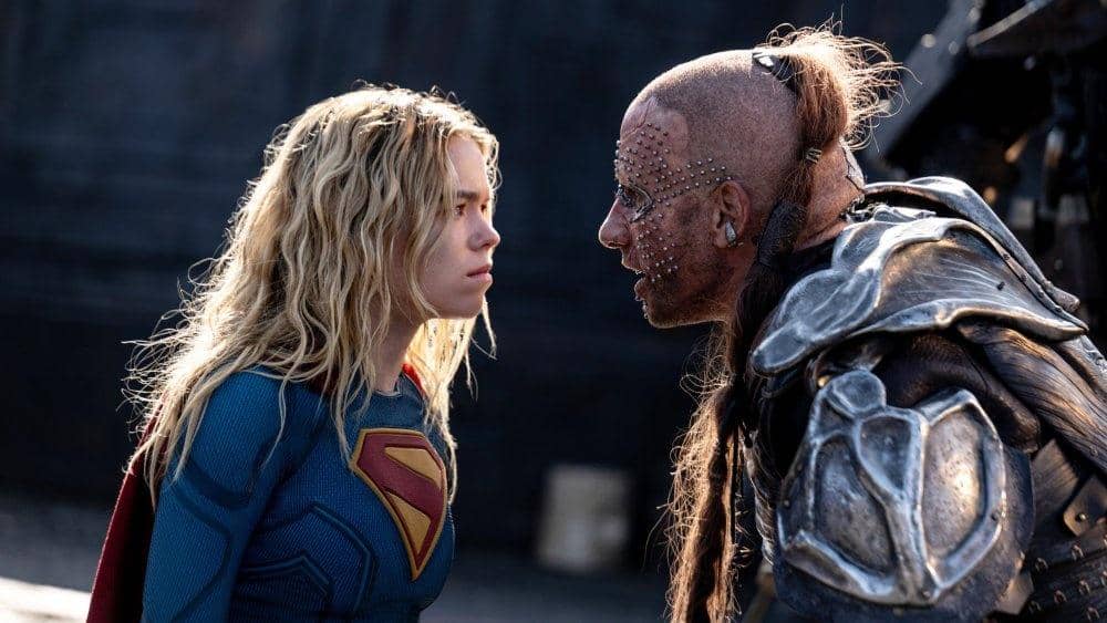 Supergirl berhadapan dengan pria berzirah logam dan wajah penuh tindikan dalam adegan intens dari film Supergirl produksi DC Studios.