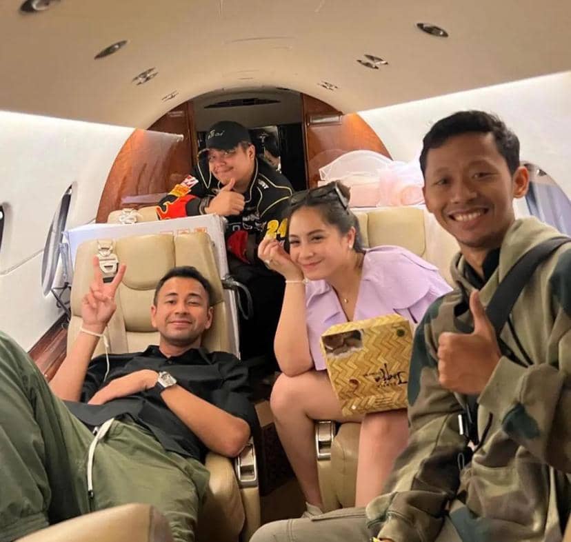 Empat orang tersenyum dan berpose santai di dalam kabin jet pribadi dengan kursi kulit berwarna krem dan pencahayaan hangat.