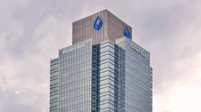 Gedung tinggi dengan logo dan nama Permata Bank di bagian atas fasad kaca modern di bawah langit berawan.