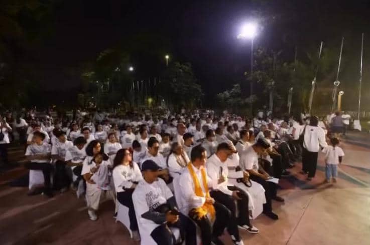 Ratusan orang mengenakan pakaian putih duduk bersama di area terbuka pada malam hari untuk mengikuti doa bersama dengan suasana khidmat.