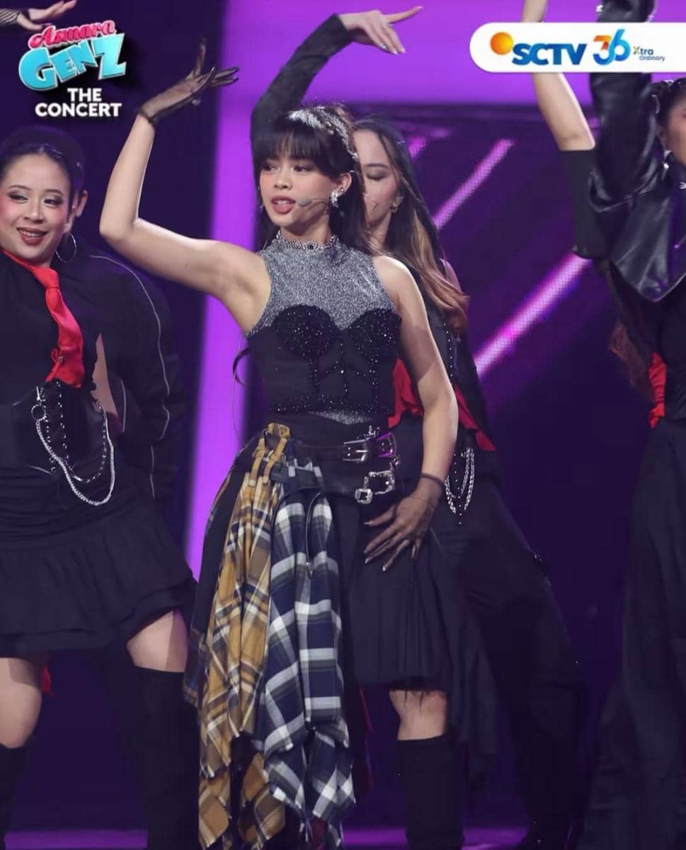Seorang penyanyi muda tampil energik di atas panggung Asmara Gen Z The Concert dengan busana hitam dan kemeja kotak-kotak di pinggang.