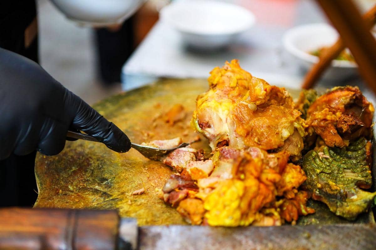 Potongan ayam ungkep bumbu kuning sedang dipotong di atas talenan besar dengan warna kuning keemasan yang menggugah selera.