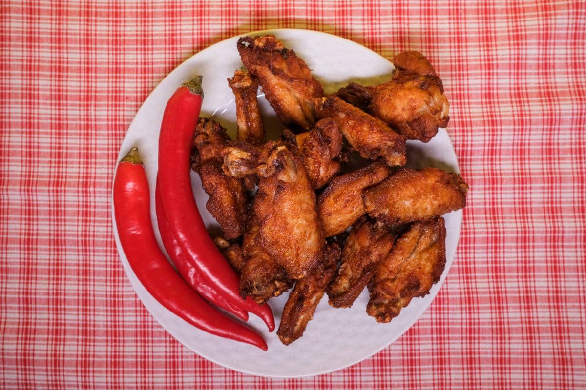 Sepiring ayam woku goreng berwarna keemasan disajikan dengan cabai merah besar di atas kain bermotif kotak merah putih.