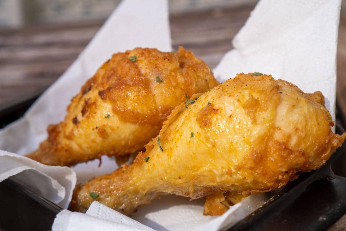 Dua potong ayam goreng bumbu Bali berwarna keemasan disajikan di atas tisu putih di atas nampan hitam.