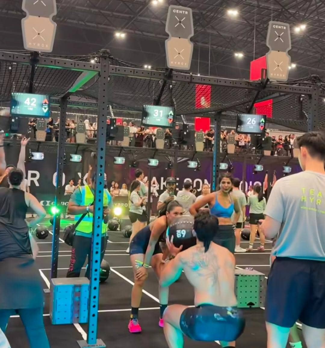 Peserta melakukan latihan fisik intens di arena kompetisi Hyrox indoor dengan suasana ramai dan pencahayaan berwarna hijau.