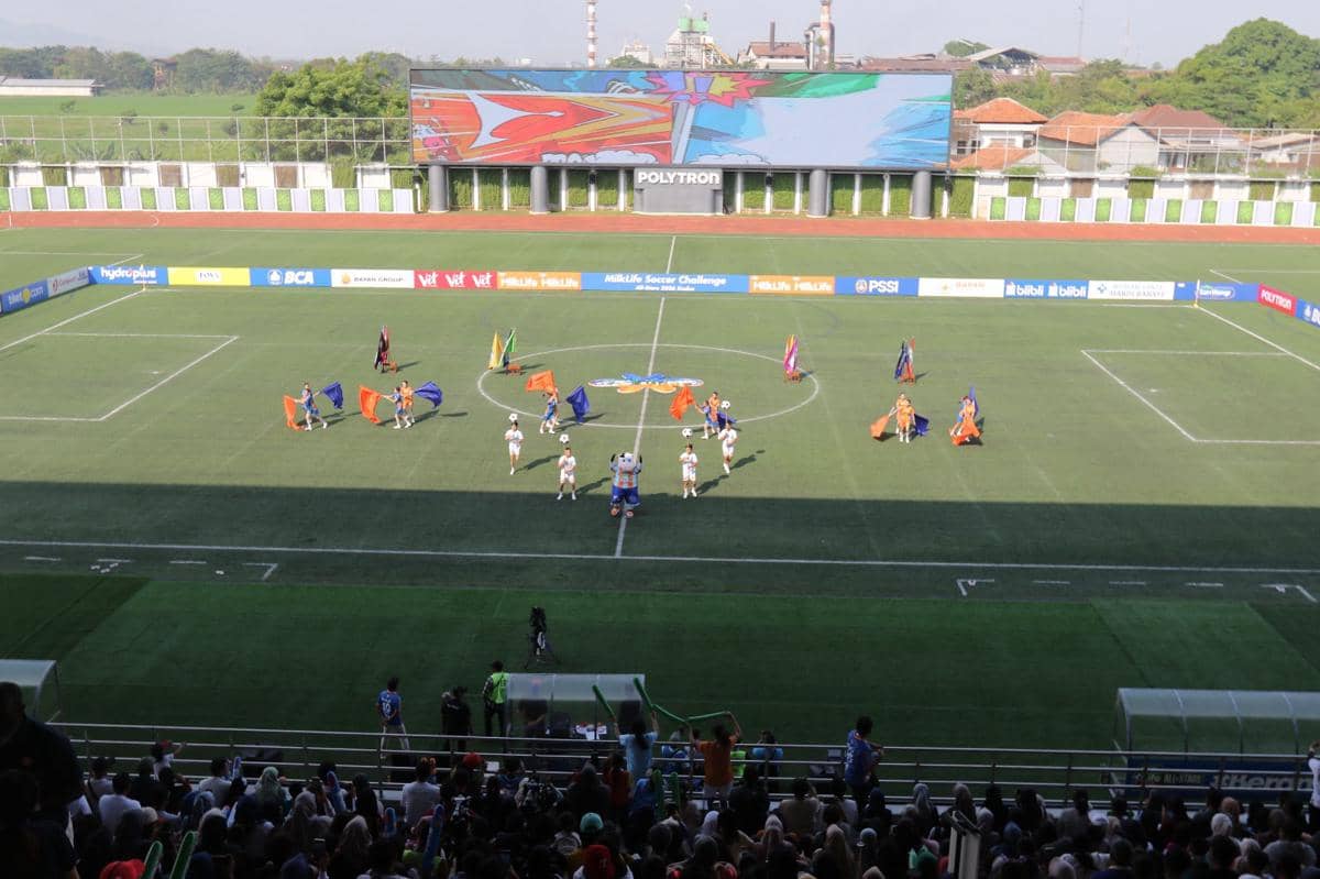 Pertunjukan pembuka di tengah lapangan sepak bola dengan penari membawa bendera warna-warni pada acara MLSC All Stars 2026.