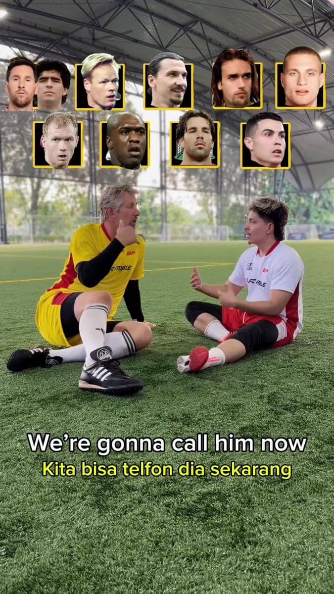 Dua pria duduk di lapangan sepak bola dalam ruangan sambil berbincang, mengenakan seragam olahraga kuning dan putih merah dengan teks di layar.