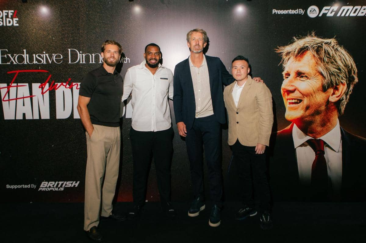 Empat pria berpose di depan latar bertuliskan acara eksklusif dengan Edwin van der Sar, salah satunya mengenakan jas biru tua.