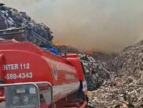 Mobil pemadam kebakaran beroperasi di area TPA Jatiwaringin yang terbakar, dengan asap tebal membubung di antara tumpukan sampah.