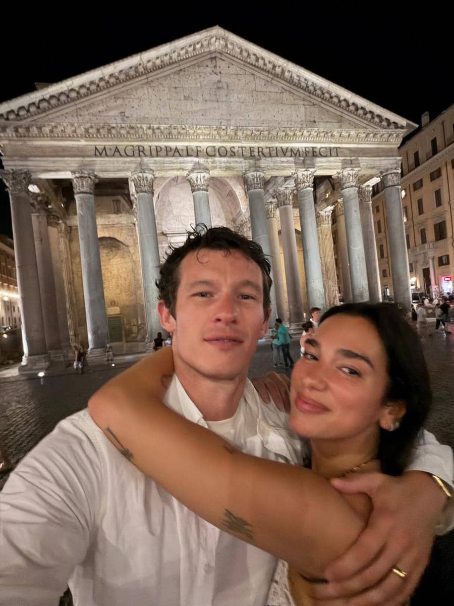 Sepasang kekasih berpose berpelukan di depan bangunan bersejarah Pantheon Roma pada malam hari dengan pencahayaan hangat.