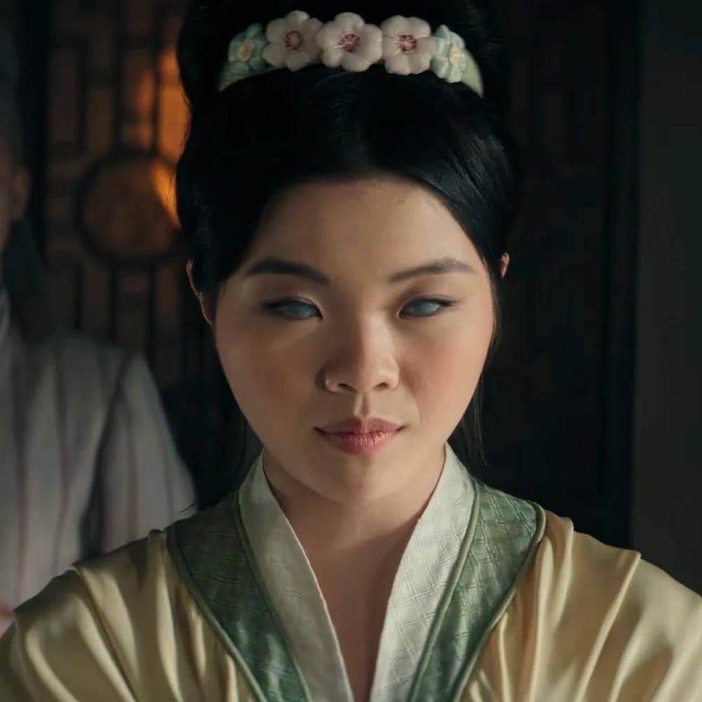 Seorang perempuan berambut hitam dengan mata berwarna pucat mengenakan pakaian tradisional dan hiasan bunga di rambutnya dalam adegan Avatar: The Last Airbender Season 2.