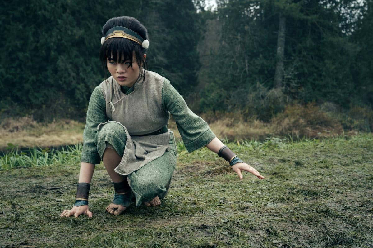 Seorang karakter berpakaian hijau dan abu-abu berlutut di tanah berlumpur dengan latar hutan dalam adegan Avatar: The Last Airbender Season 2.