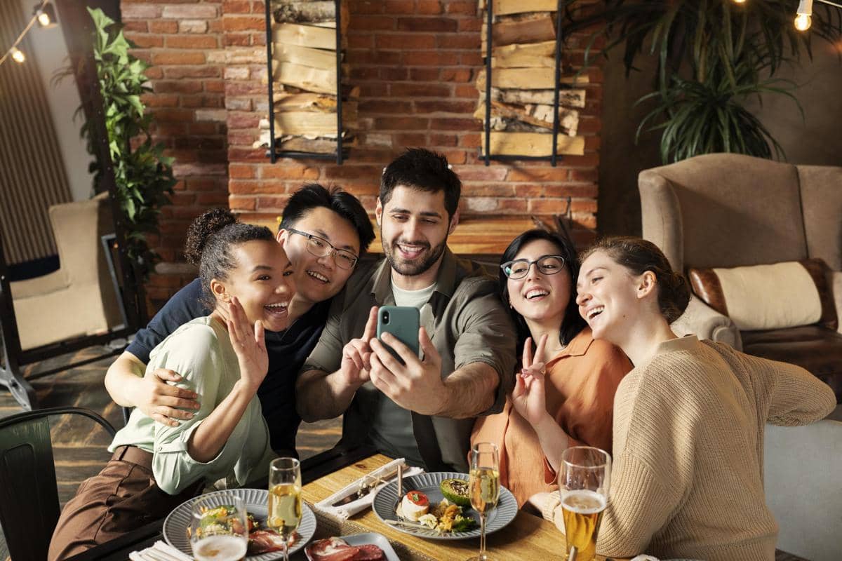 Sekelompok teman tersenyum dan berfoto bersama di restoran dengan suasana hangat dan makanan di atas meja.