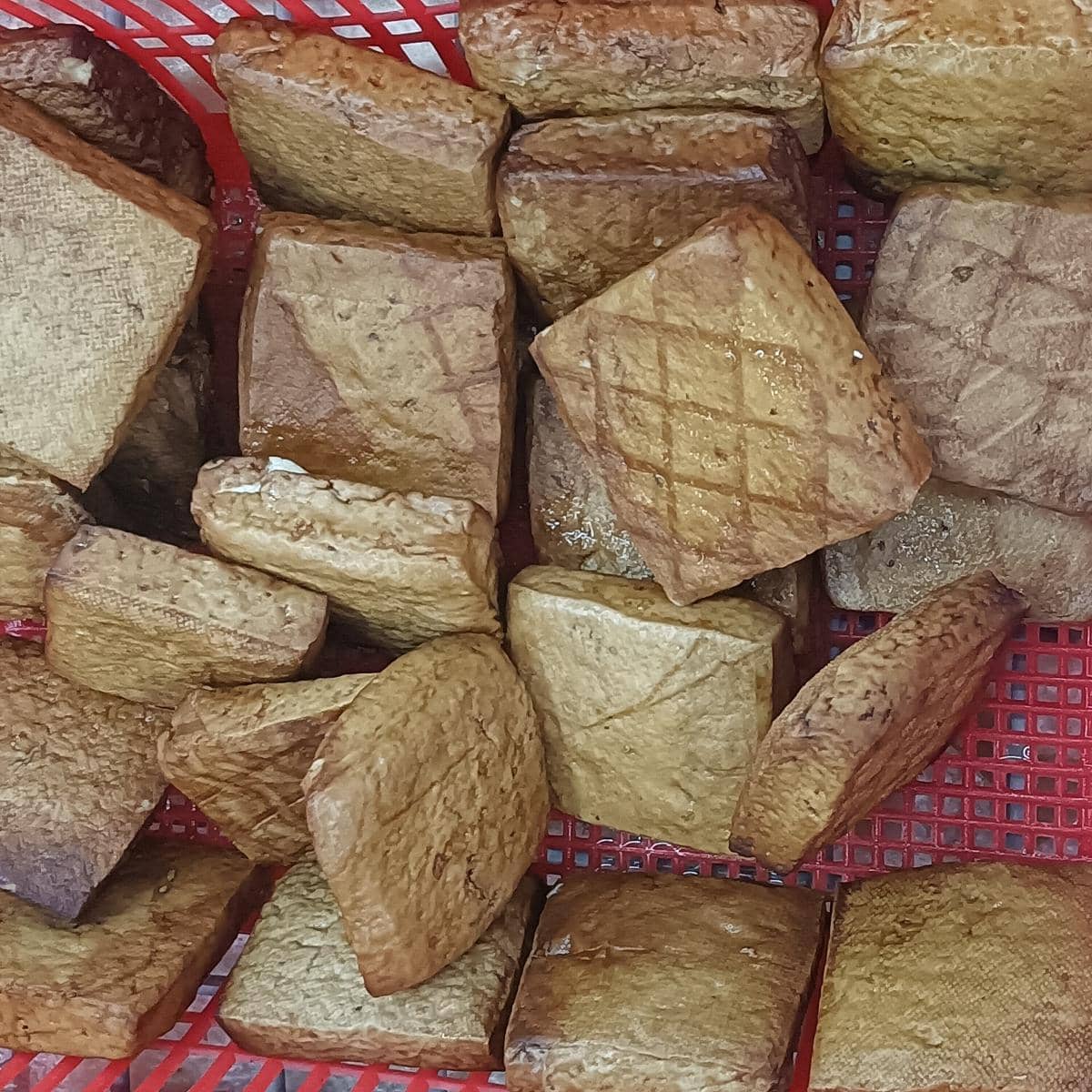 Potongan dougan berwarna cokelat keemasan dengan tekstur padat tersusun dalam wadah anyaman plastik merah.