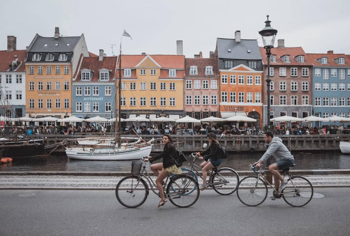 Beberapa orang bersepeda di tepi kanal dengan deretan bangunan berwarna-warni di kawasan Nyhavn, Copenhagen, Denmark.