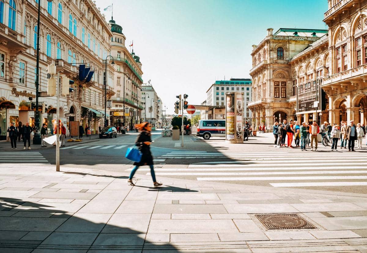 Suasana jalanan di pusat kota Vienna, Austria, dengan bangunan bergaya klasik, pejalan kaki, dan kendaraan di persimpangan kota.