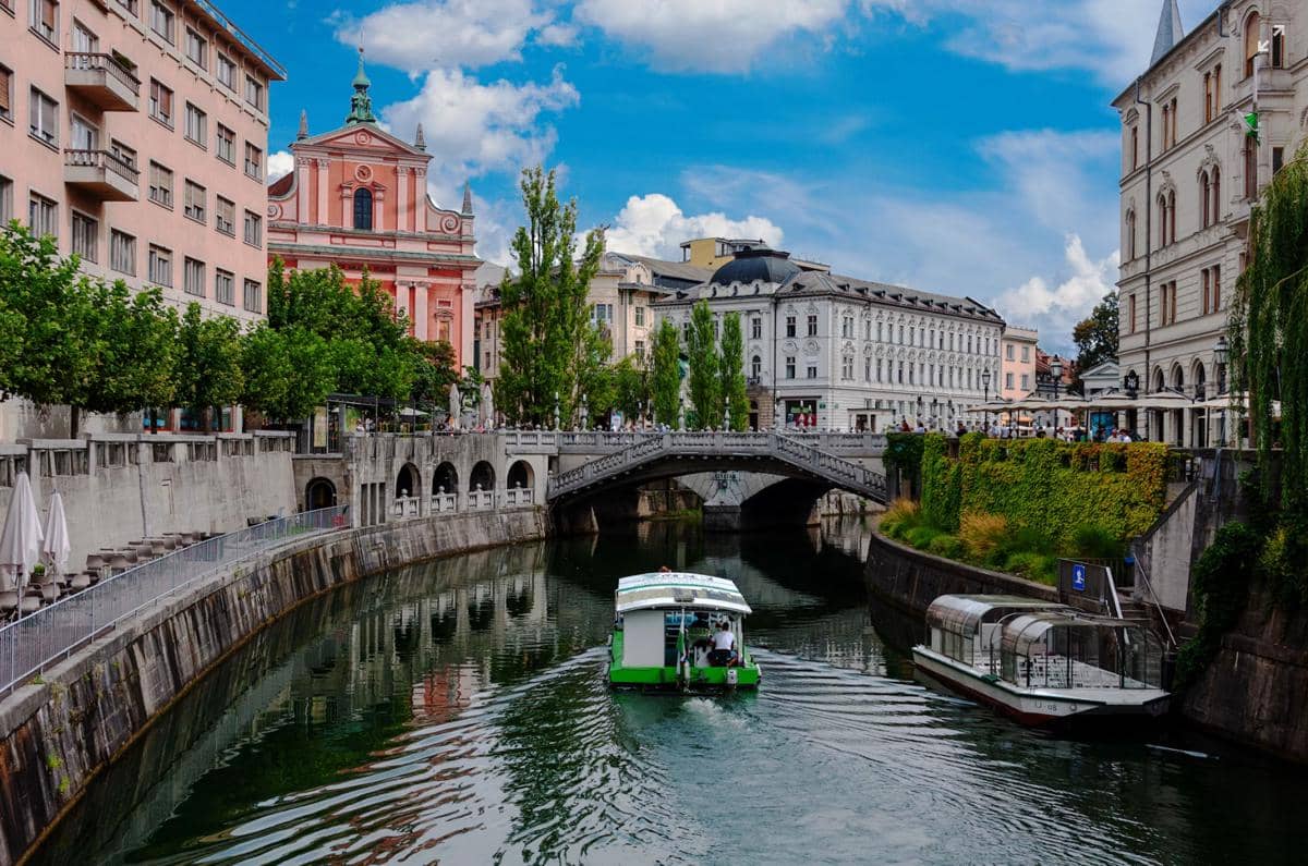 Perahu melintas di sungai yang membelah pusat kota Ljubljana, Slovenia, dengan jembatan dan bangunan berarsitektur klasik di sekitarnya.