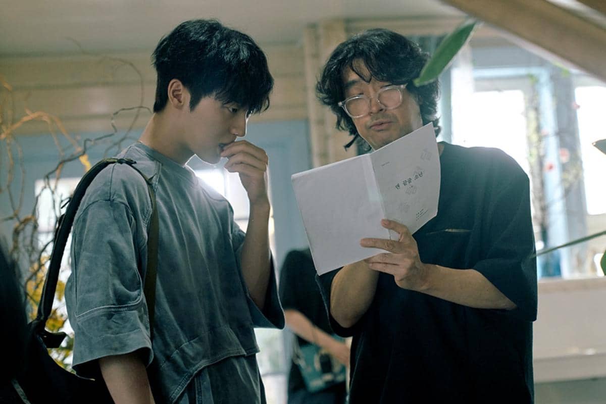 Dua pria sedang berdiskusi serius sambil memegang naskah di lokasi syuting serial Notes from the Last Row produksi Netflix.