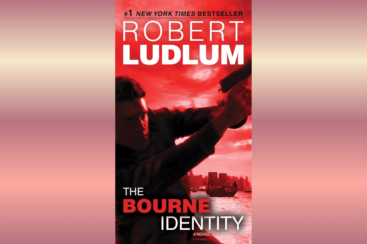 Sampul buku The Bourne Identity karya Robert Ludlum dengan latar merah menampilkan sosok pria memegang senjata di tepi laut.