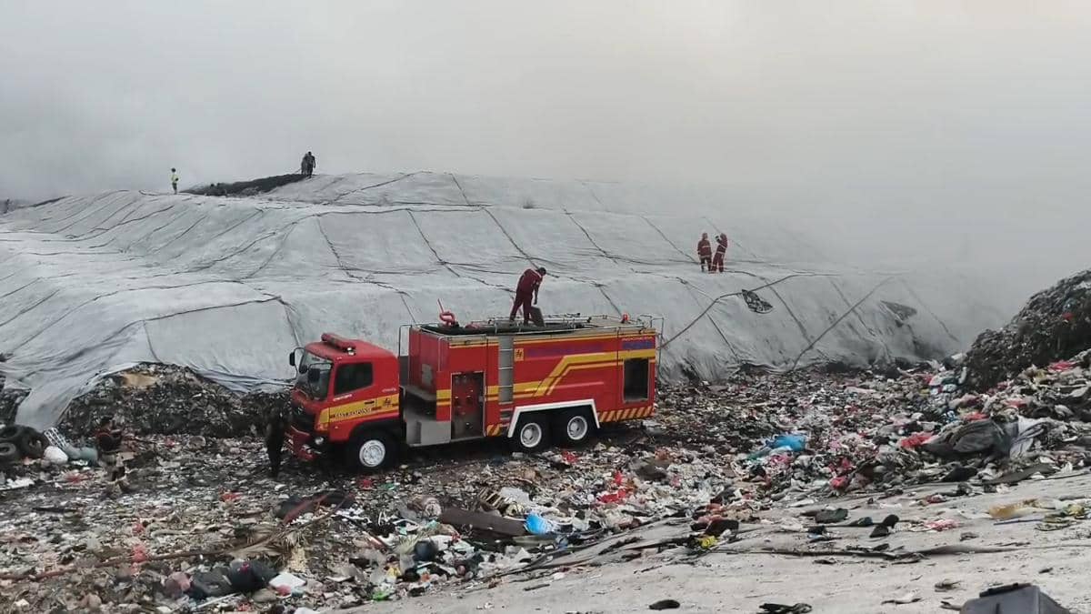 Mobil pemadam kebakaran dan petugas berupaya memadamkan api di area TPA Jatiwaringin yang tertutup asap tebal dan tumpukan sampah.