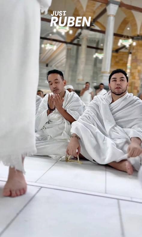 Dua pria mengenakan pakaian ihram putih sedang duduk dan berdoa di dalam masjid saat melaksanakan ibadah umrah.