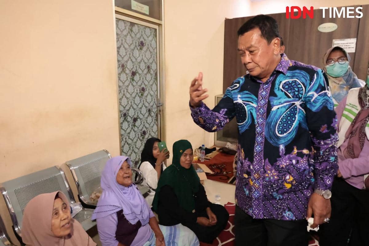 Seorang pejabat daerah berbicara dengan warga yang mengungsi di dalam ruangan, beberapa perempuan duduk mendengarkan dengan perhatian.