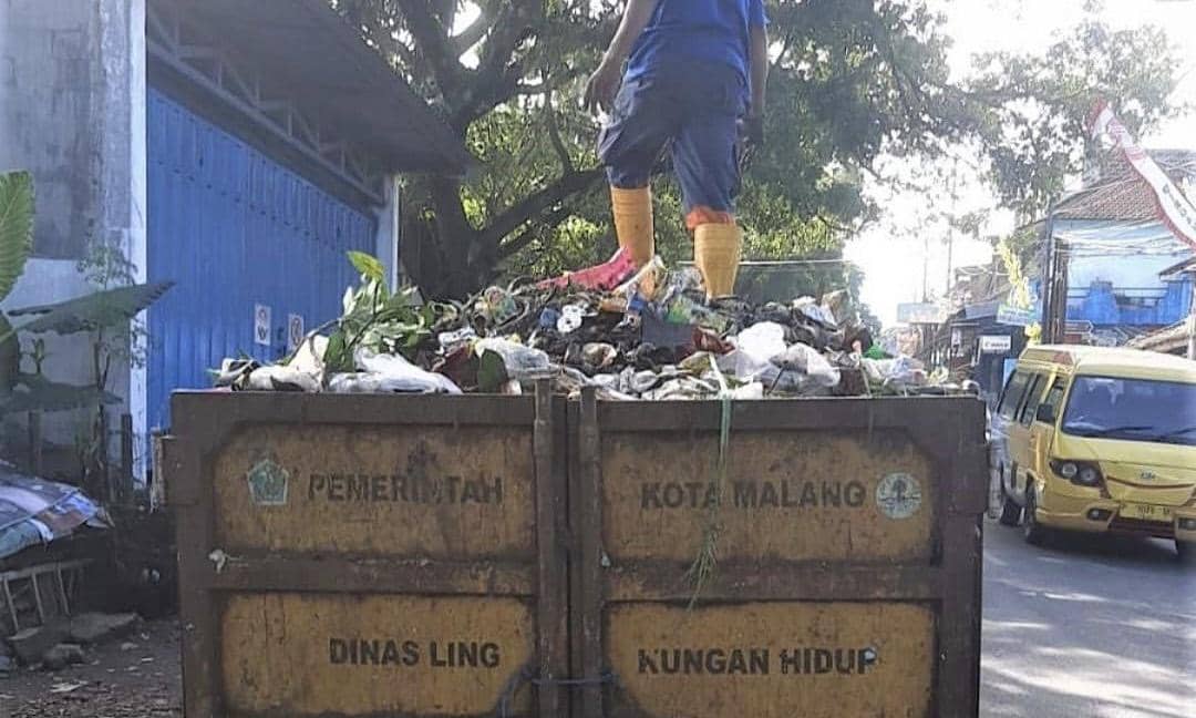 Petugas kebersihan berdiri di atas truk pengangkut sampah milik Dinas Lingkungan Hidup Kota Malang yang penuh dengan sampah dan dedaunan.
