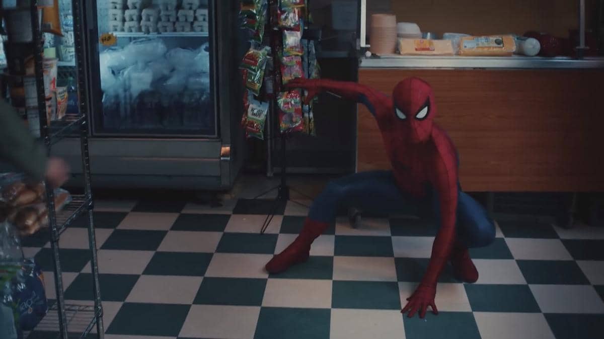 Spider-Man berpose siap bertarung di dalam toko kecil dengan lantai kotak-kotak hitam putih dan rak berisi makanan ringan.